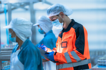 Supervisor in orange uniform and hairnet inspects canned food on the production line with factory...
