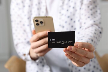 Woman with credit card and smartphone paying online on blurred background, closeup