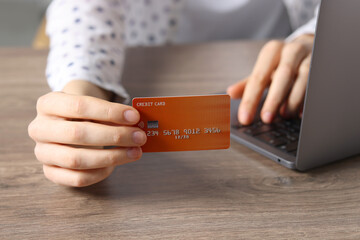 Online payment. Woman with credit card and laptop at wooden table, closeup