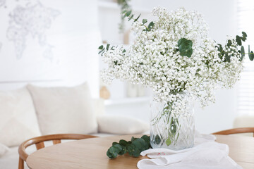Bouquet of beautiful gypsophila flowers and eucalyptus branches in vase on table indoors. Space for...