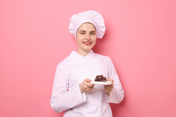 Confectioner in uniform holding delicious chocolate dessert on pink background
