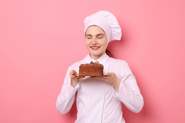Confectioner in uniform holding delicious chocolate cake on pink background