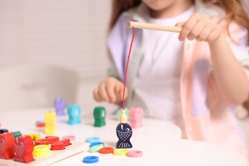 Motor skills development. Little girl playing with math game Fishing for Numbers at white table indoors, closeup