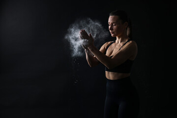 Woman clapping hands with talcum powder before training on black background, space for text