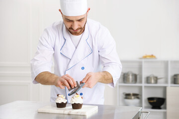 Confectioner grating chocolate onto cupcake at table in kitchen, space for text