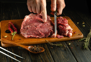 A person skillfully slices raw meat on a wooden cutting board, surrounded by herbs, spices, and a...