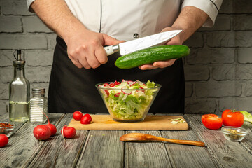 In a cozy kitchen, a chef skillfully slices a cucumber above a bowl of fresh salad. Colorful tomatoes and radishes enhance the vibrant display while seasonings await