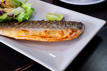 Grilled mackerel served on a white plate with fresh green salad, topped with creamy dressing and a slice of lime. A healthy and delicious seafood dish perfect for food content