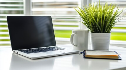 Minimalist desk setup with closed laptop, potted plant, notebook, and mug on a clean white surface