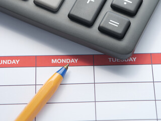 A weekly schedule with a ballpoint pen and a calculator lying on it. Close up.