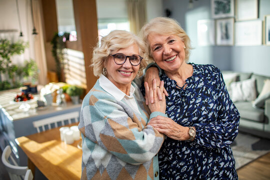 Happy senior women best friends hugging and smiling at home