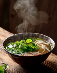 A close-up shot of a steaming bowl of pho with fresh herbs, placed on a rustic wooden table.