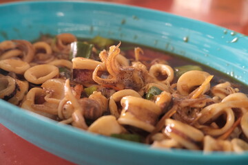 Delicious stir-fried squid in sweet soy sauce with green chili, served in a blue oval plate, capturing the essence of traditional Indonesian seafood cuisine