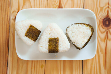 Onigiri made of rice and nori seaweed are spun on a white plate.