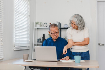 Obraz premium Elderly couple working together on laptop and documents at home, showing focus and collaboration in bright room