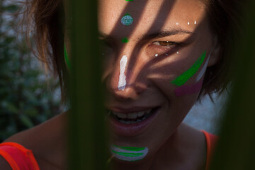 Detailed close up of beautiful woman with neon creative painting on the face. Strong shadow of palm...