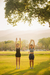 Two young Asian women exercising under a tree in the evening with beautiful golden sunlight....