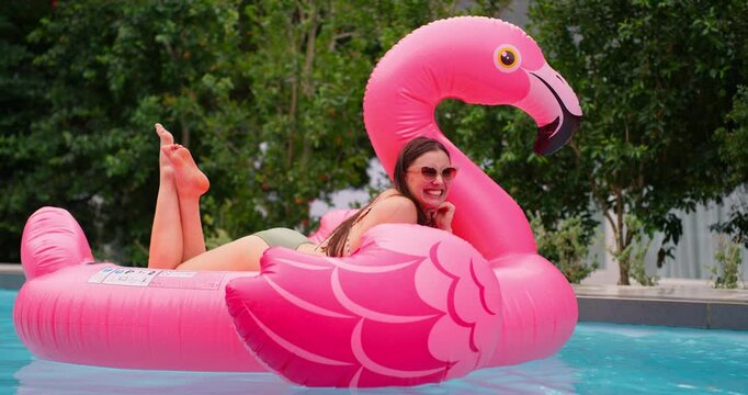 Summer, relax and woman in pool with inflatable, smile and float in water with flamingo at resort. Holiday, weekend and happy girl swimming at hotel with sunglasses, hospitality and fun vacation trip