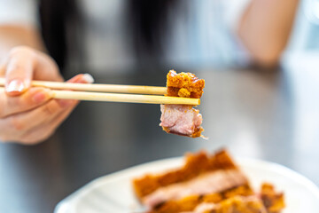 Young woman is picking up crispy pork with chopsticks in a Chinese restaurant.