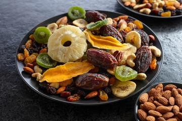 Dried tropical fruits, nuts, and raisins in black plate.
