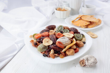 Mix of dried tropical fruits, nuts, and raisins on a white table.