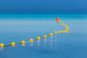 Swimming area boundary with bright yellow buoys on turquoise calm sea water on sunny day
