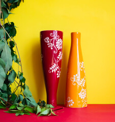 Dos jarrones de cerámica, uno amarillo y otro rojo, con intrincados diseños florales blancos...