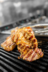 Close-up of grilled meat being lifted with tongs off a sizzling grill, showcasing beautifully charred marks and rich color, emphasizing the cooking process in a professional kitchen.