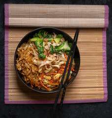 Vegan stir fry consisting of yuba, carrot, bok choy and noodles, served in black bowl