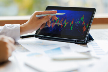 Focused on strategy, an investor holds a market analysis report, assessing stock performance with a tablet displaying real-time fluctuating graphs beside them.