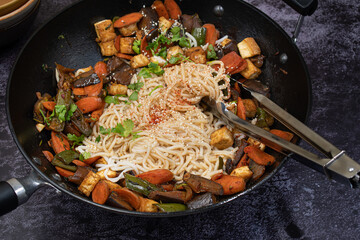 Vegan Stir fried eggplant, carrot and pepper served with rice noodles in cast iron wok