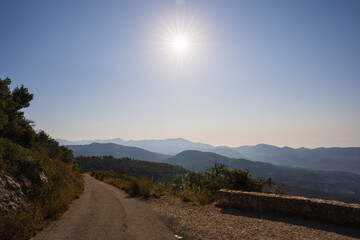 Picturesque mountain landscape near Nice, France, with a winding road under bright sunlight and clear blue sky.