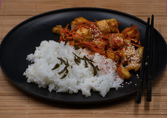 Vegan Korean tofu and kimchi, rice on black plate on bamboo mat