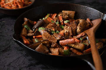 Vegan Korean seitan, carrot and eggplant fry over rice with kimchi in a black bowl