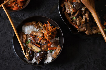Vegan Korean seitan, carrot and eggplant fry over rice with kimchi in a black bowl
