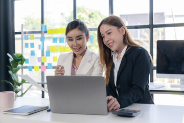 Two Asian businesswomen are discussing their business. While pointing at the graphs and charts on the table, enjoy the success and teamwork in business analysis.