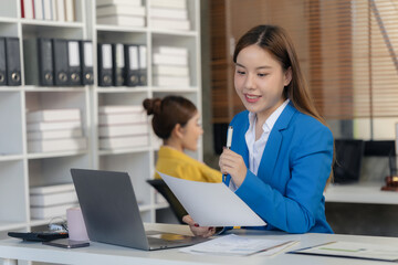 Obraz premium Two Asian businesswomen are discussing their business. While pointing at the graphs and charts on the table, enjoy the success and teamwork in business analysis.