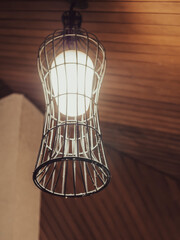 Industrial-style pendant light with a metal cage design hanging against a wooden backdrop, creating a modern yet rustic aesthetic.