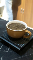 A close-up shot of a brown ceramic cup filled with freshly brewed black coffee, placed on a textured black mat over a black marble table