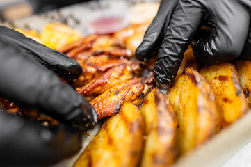 Close-up of hands in black gloves carefully selecting crisp, grilled potato wedges, showcasing...