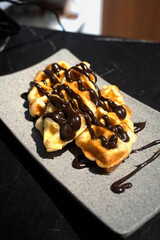 Freshly baked Belgian waffles generously drizzled with rich melted chocolate, served on a stylish gray plate over a black marble table