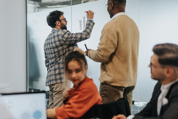 A diverse group of colleagues brainstorming and sharing ideas in an office setting. Creative teamwork and collaboration are evident as they work on a project using a whiteboard.