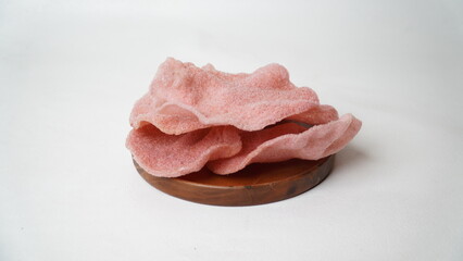 Kerupuk merah, red crackers are crispy red snacks often served as a food complement. Served on wooden plate isolated on white background.