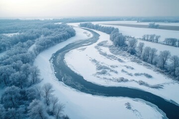 An aerial view reveals a river winding through a snowy, frost-covered landscape on a serene winter day.