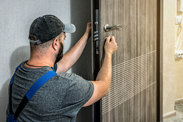 Professional locksmith in blue overalls repairing home entrance door lock
