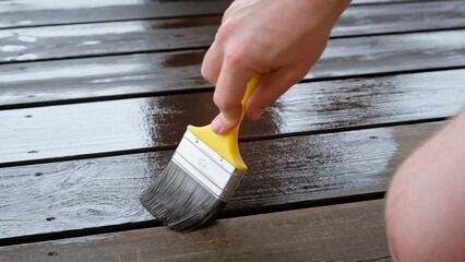 Close-up of a brush painting wood floor in brown color. Wood plank impregnation. Finish oil coating...