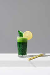 Jugo de espinacas adornado con una rodaja de limón y hoja de espinaca sobre una mesa blanca y...