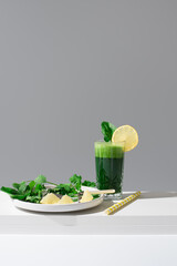 Jugo de espinacas adornado con una rodaja de limón y hoja de espinaca sobre una mesa blanca y...