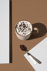Café servido en taza con crema de leche y fideos de chocolate sobre fondo marrón y blanco	