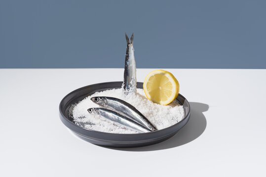 Tres anchoas frescas con lim&oacute;n sobre un plato lleno de sal sobre fondo azul	